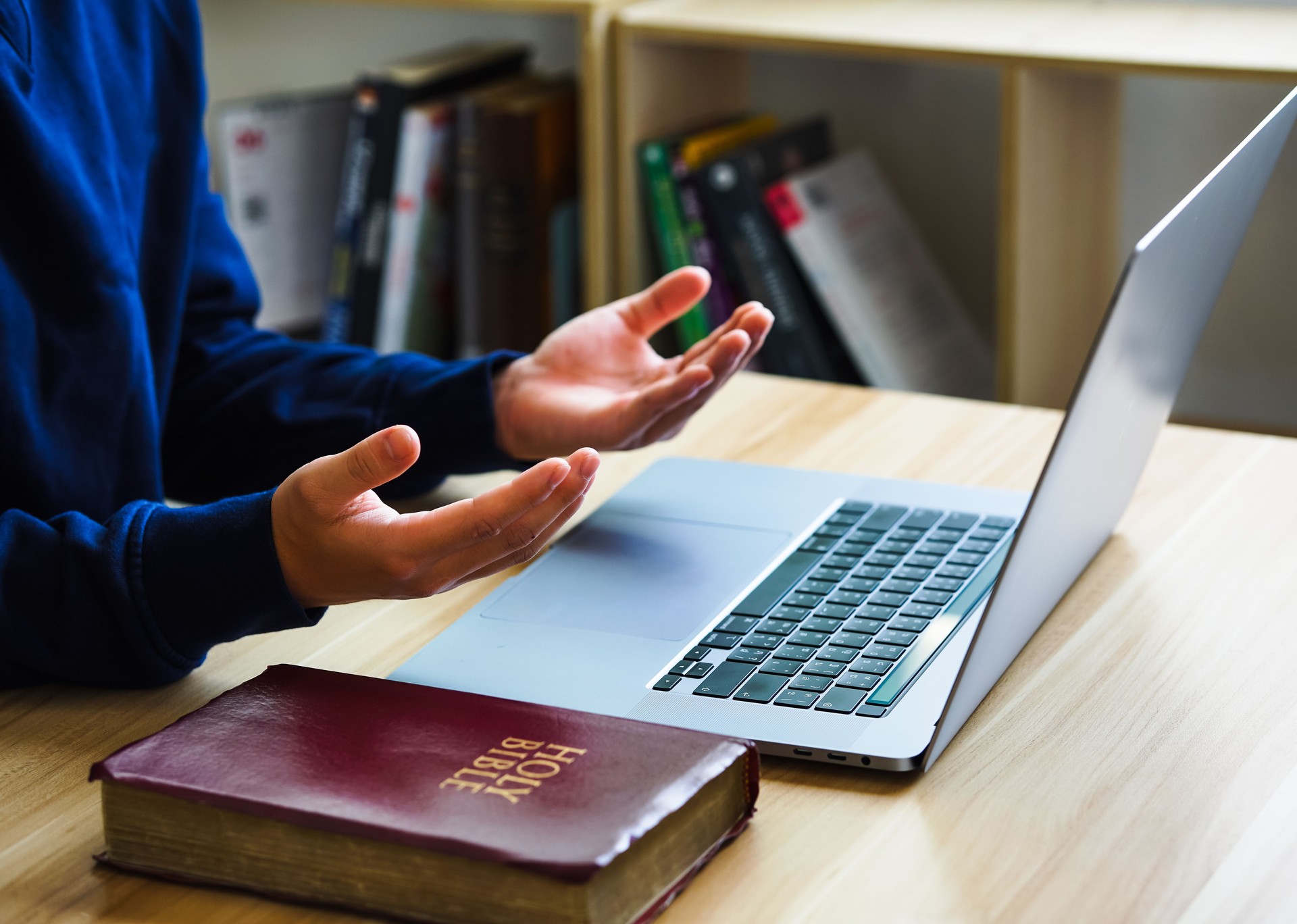 Hands holding a bible placed on a laptop were opened for learning to understand the Bible in order to pray to God and to ask God to protect himself and his family. Online bible.